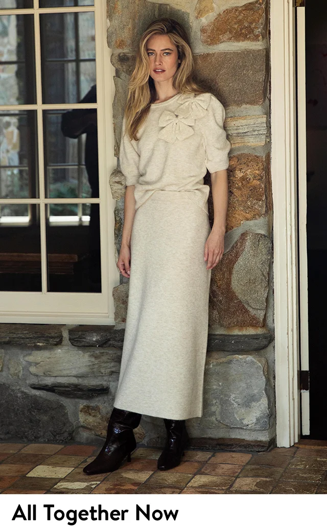 A woman wearing a puff-sleeve sweater with a bow detail and matching skirt.