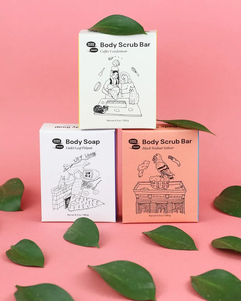 Three boxes of soap are stacked with bright green leaves arranged around them