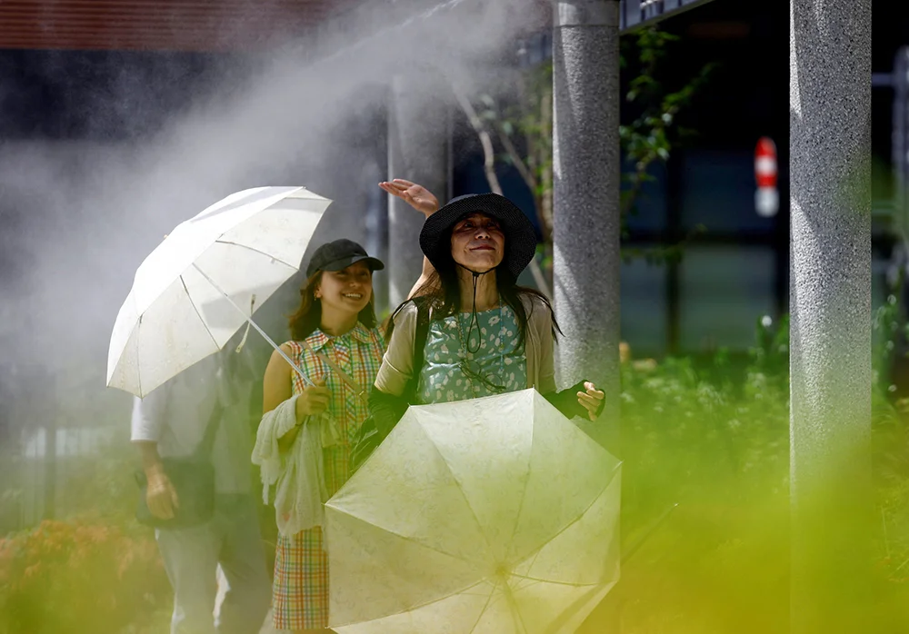 Two women carrying parasols as they walk through misters during a heatwave in Japan