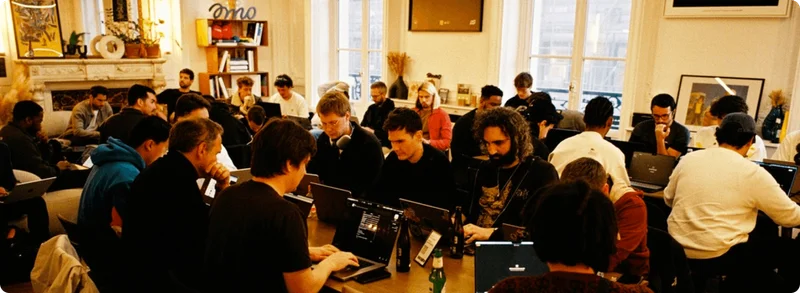 A diverse group of people are working on laptops in a bright, open-plan office space.