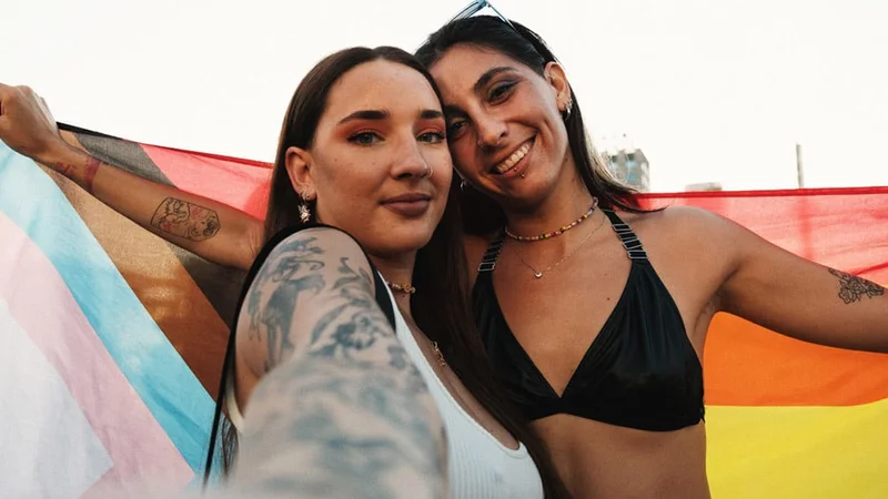 Image description: Two people with a pride flag wrapped around them