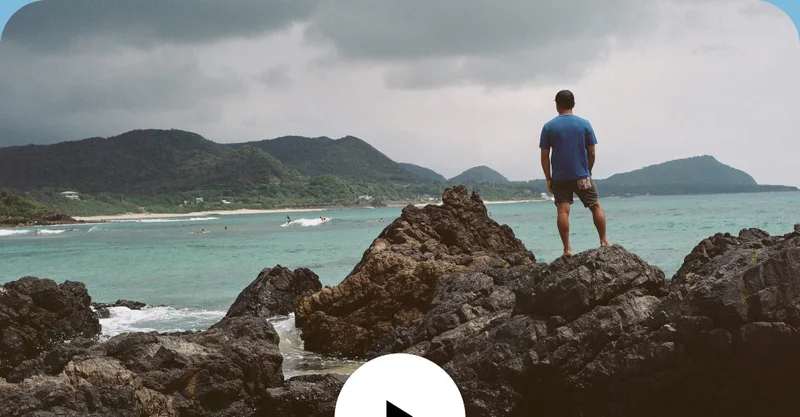 A person stands on rocks overlooking the ocean.