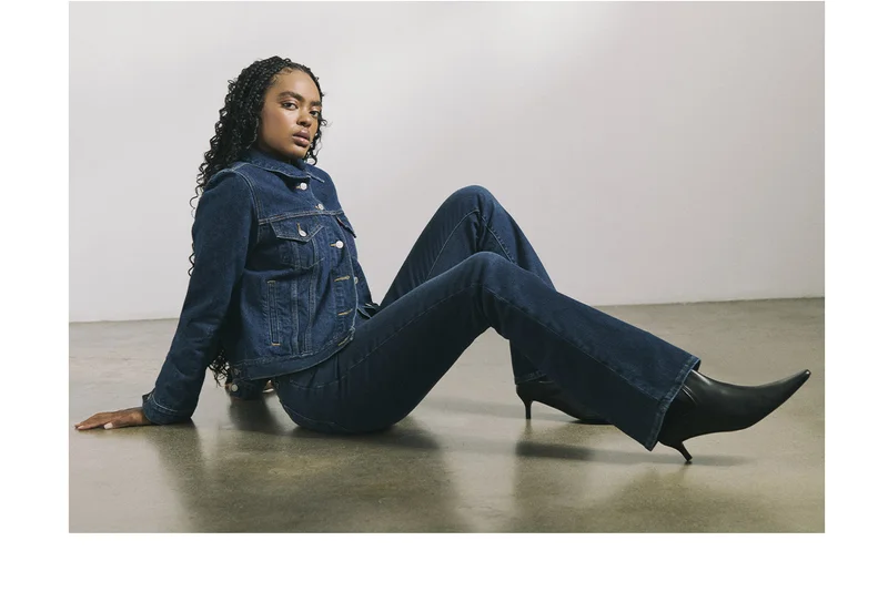 Woman sitting on the ground wearing a dark wash trucker jacket and jeans.