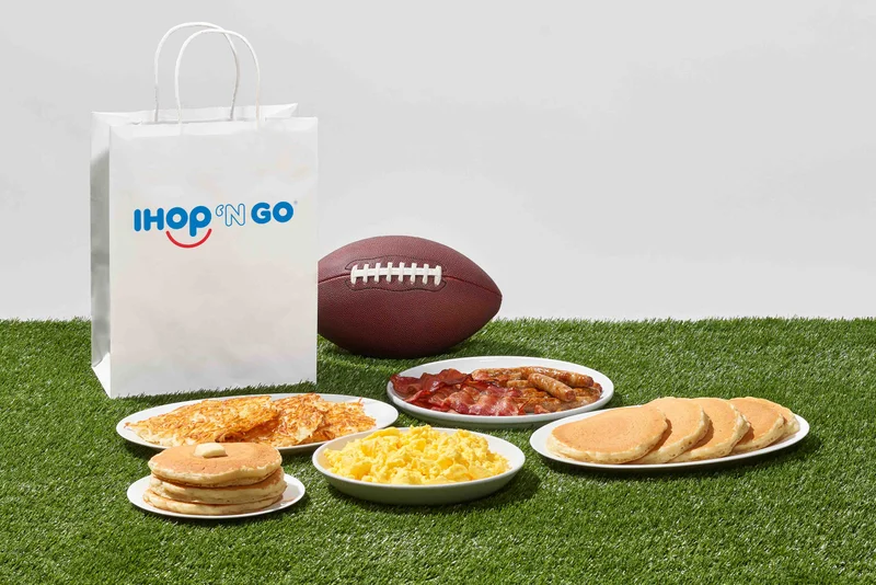 Plates of IHOP food are on turf, along with a football and to go bag.