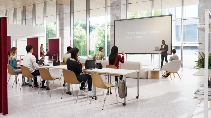 A teacher presenting at a podium in front of a small class in a large, bright, open room.