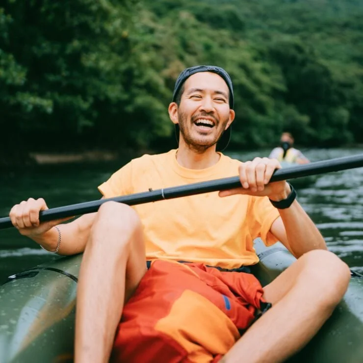Person laughing whilst kayaking down river with a friend kayaking behind them.