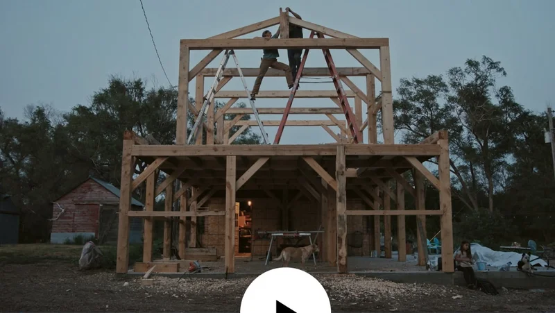 Two people stand on ladders on the second floor of a timber-frame build.
