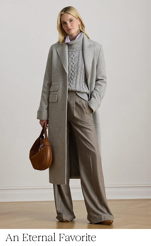 A woman wearing a sweater, wool coat and trousers, carrying a handbag.