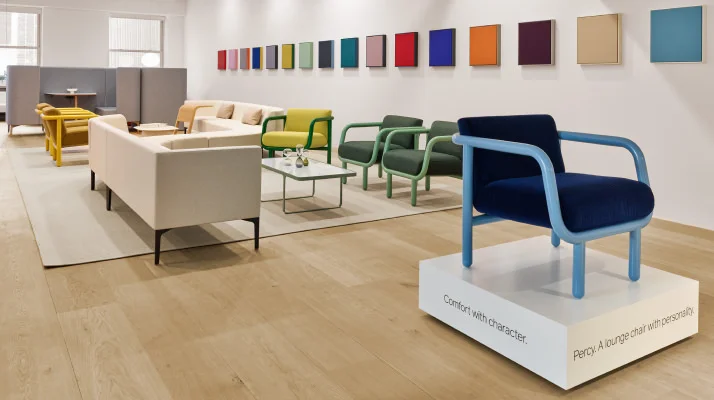 A showroom setting with a Percy chair in dark blue upholstery with light blue arms featured prominently on a white platform.