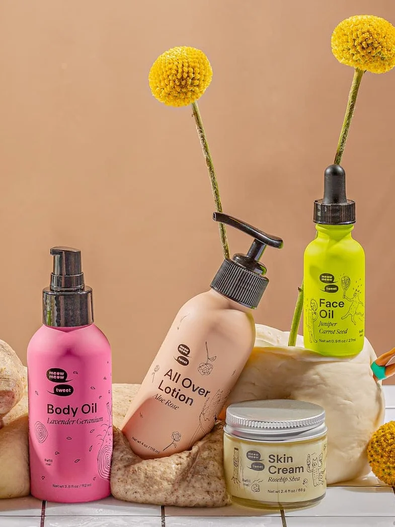 Four skincare products in colorful packaging are nestled into globs of dough and flowers.