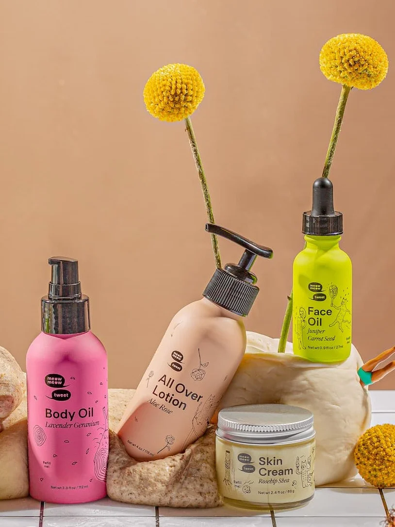 Four skincare products in colorful packaging are nestled into globs of dough and flowers. Four skincare products in colorful packaging are nestled into globs of dough and flowers.