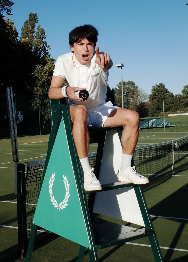 Snake Denton speaks to the rising stars of British tennis. In the image, he sits on an umpire stand on a tennis court and points directly at the camera.