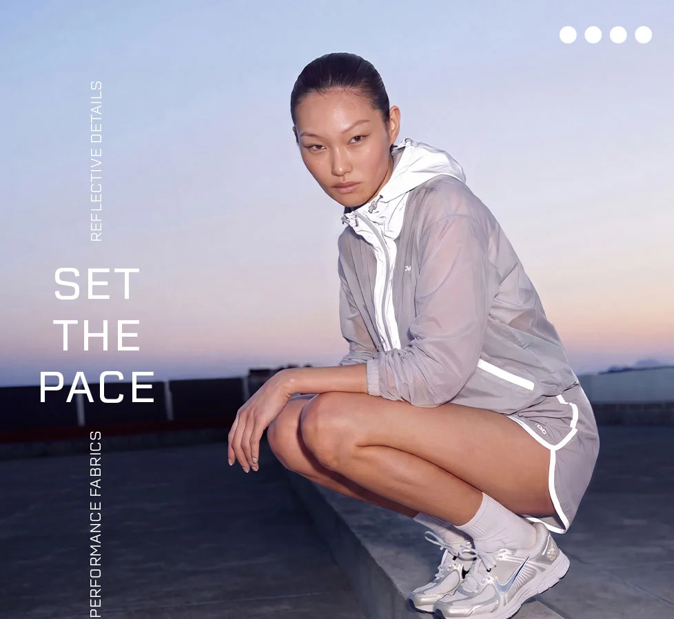Woman in reflective windbreaker jacket & running shorts. Performance activewear with reflective details for setting the pace.