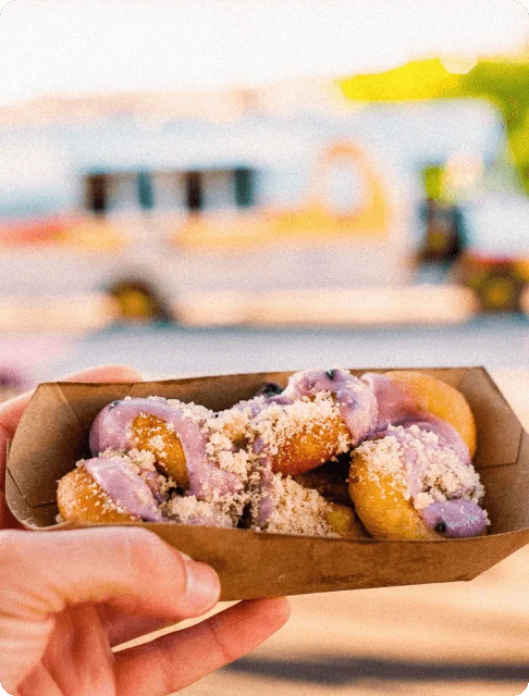Image Description: A paper food tray of cinnamon donut holes slathered in purple cream