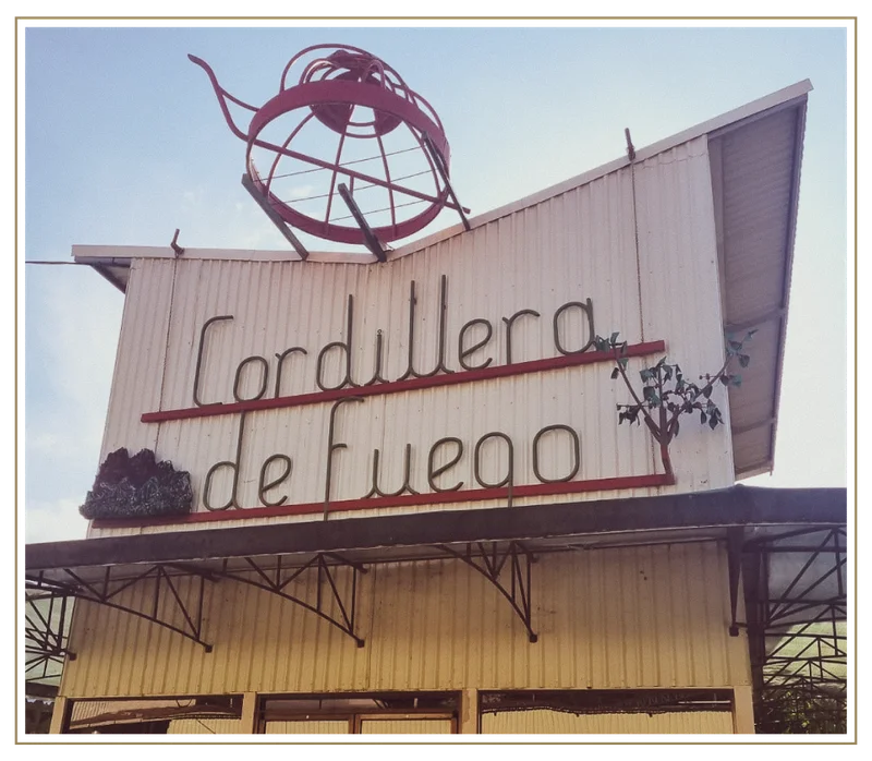 Exterior view of the Cordillera de Fuego coffee mill facility in Costa Rica, featuring a large retro-style sign mounted on the building with sculptural metal artwork above it.