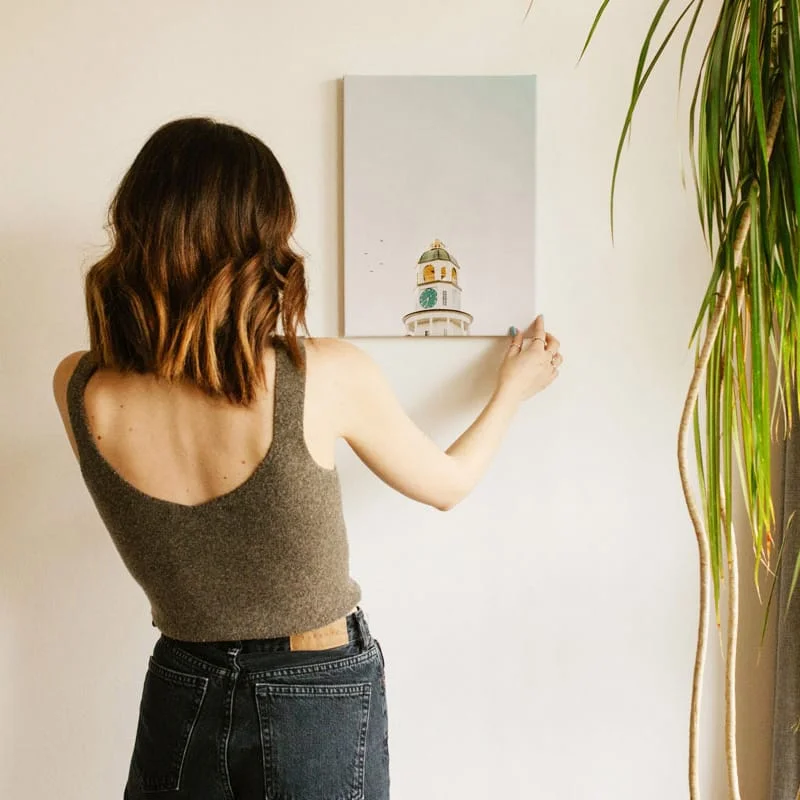 Photo of woman hanging canvas print of lighthouse on wall.