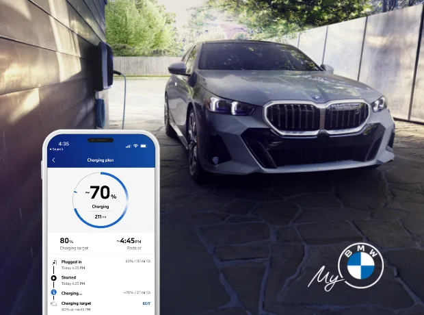 A photo of a BMW i5 sedan parked in a garage with the My BMW app showing the vehicle's charging status and trip overviews.