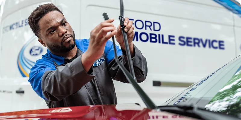 Ford Service technician adjusting a windshield wiper on a red vehicle with a Ford Mobile Service van in the background