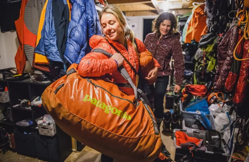 Two people sort through snow equipment in a gear room.