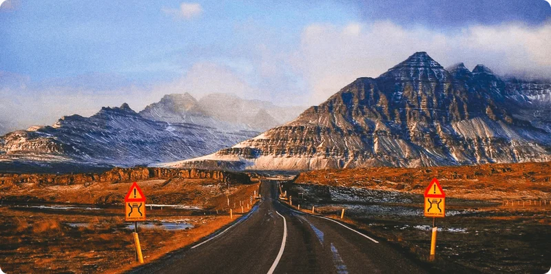 Image Description: Long, empty road with large, snow-dusted mountains in the near distance.