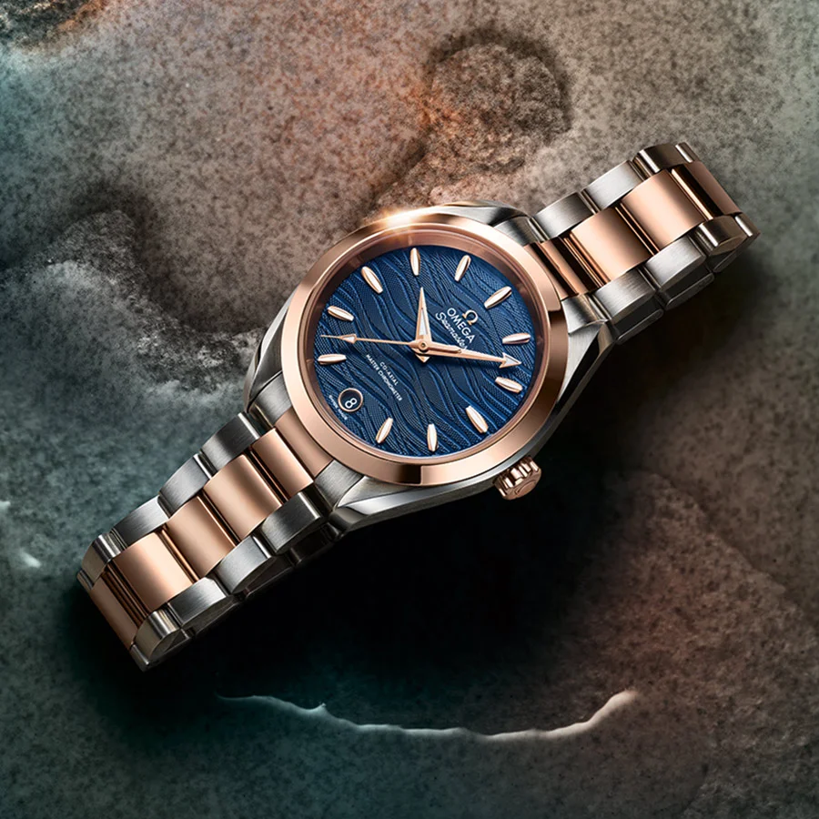 The Seamaster Aqua Terra 150M in 38 mm with a blue ocean-inspired dial and an integrated stainless-steel and 8K Sedna™ gold bracelet, displayed against a textured background.
