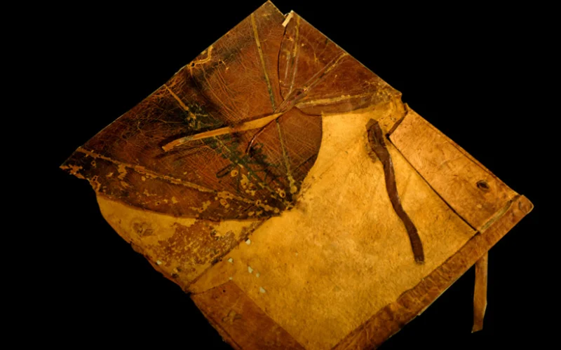 Old leather-bound book with a worn cover, frayed edges, and tie closures, set against a black background.