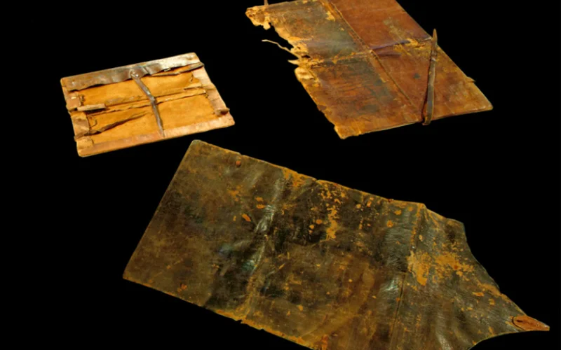 Aged, fragmented ccodex covers on a black background. The weathered leather surfaces are tinged with rich brown hues and golden textures