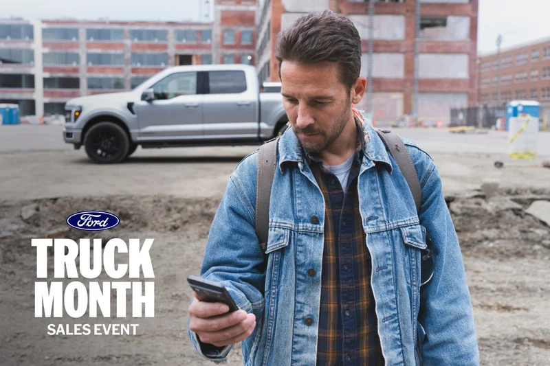 Man looking at his phone while walking away from a parked silver truck.