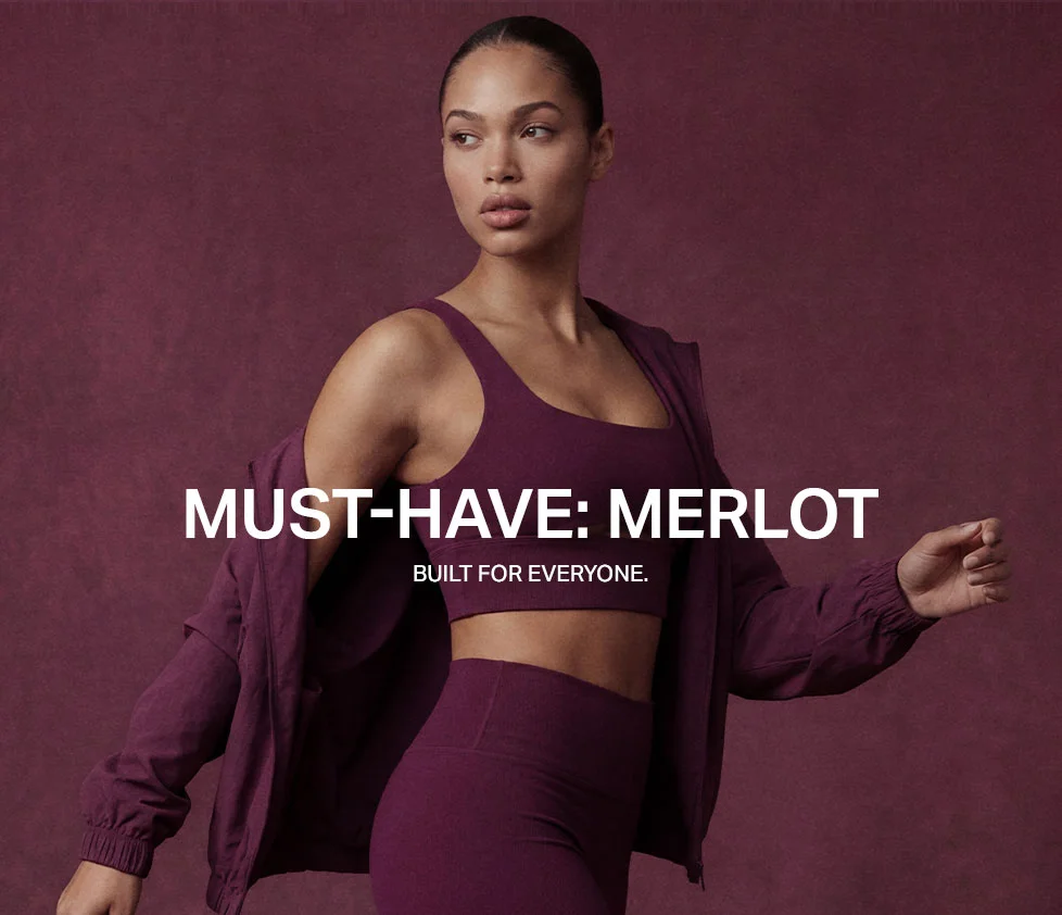 Woman in merlot activewear: sports bra, leggings, and an open jacket draped. Promoting a must-have burgundy fitness collection.