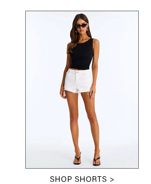 Woman models a black one-shoulder top and white frayed denim shorts with black sandals, highlighting versatile summer style. Shop shorts.
