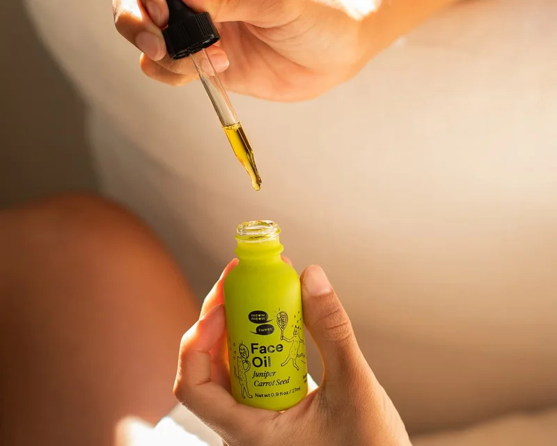 A pair of tan hands pulls a dropper of green oil out of a green bottle