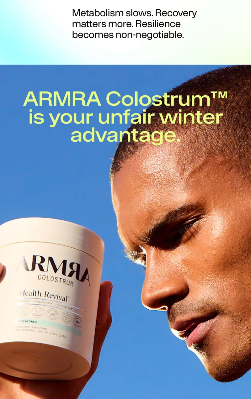 Person holding an ARMRA Colostrum jar against a blue sky, emphasizing winter performance and recovery.