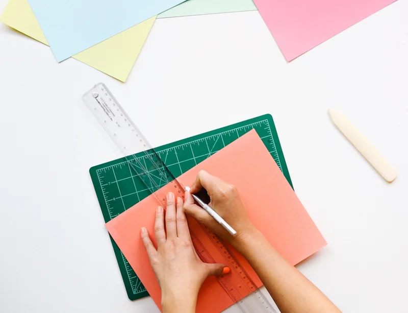 A top down photo of a person's hands cutting paper with a ruler