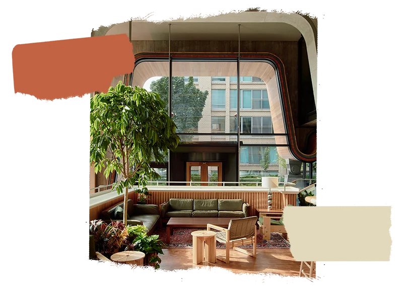 Lobby of Ace Hotel Toronto featuring an array of natural wood furnishings, indoor plants, and large, curved windows that frame a view of the bustling city outside.
