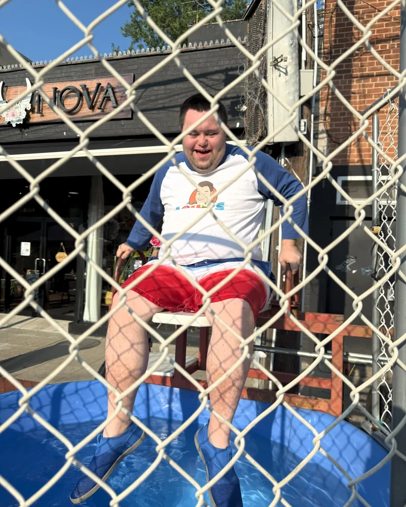 John in a white t-shit and bathing suit sitting atop a dunk tank