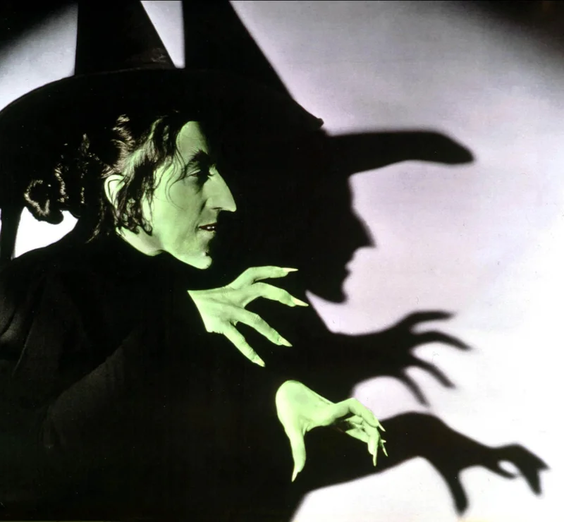 A screen-test image of actress Margaret Hamilton as The Wizard of Oz's Wicked Witch of the West, complete with pointy black hat and warts. The image is colorized to nod to the cinematic villain's iconic green skin.
