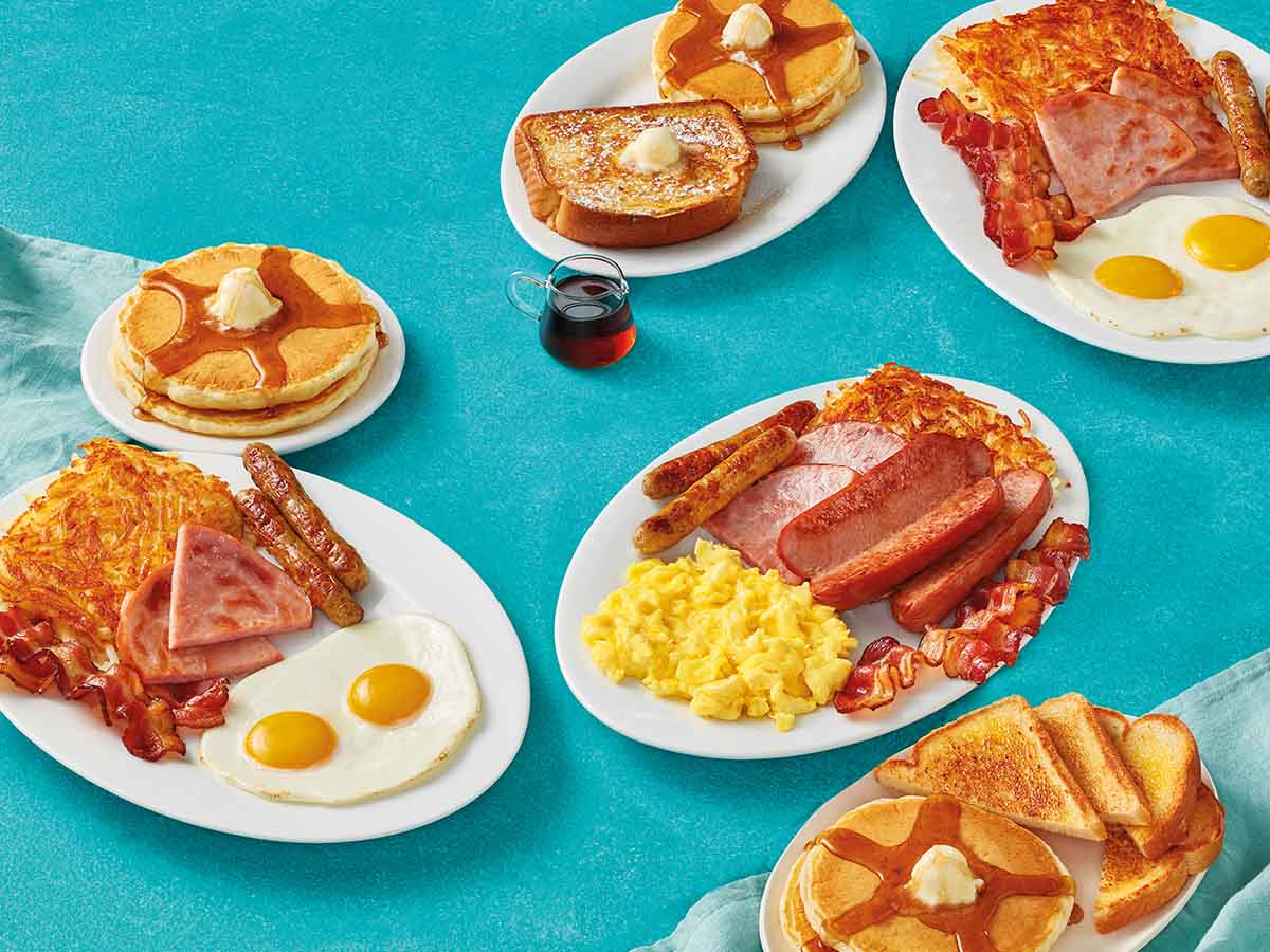 IHOPs BreakFEASTs set on a blue tabletop. Features plates of hashbrowns, eggs, bacon, sausage, pancakes, and toast.