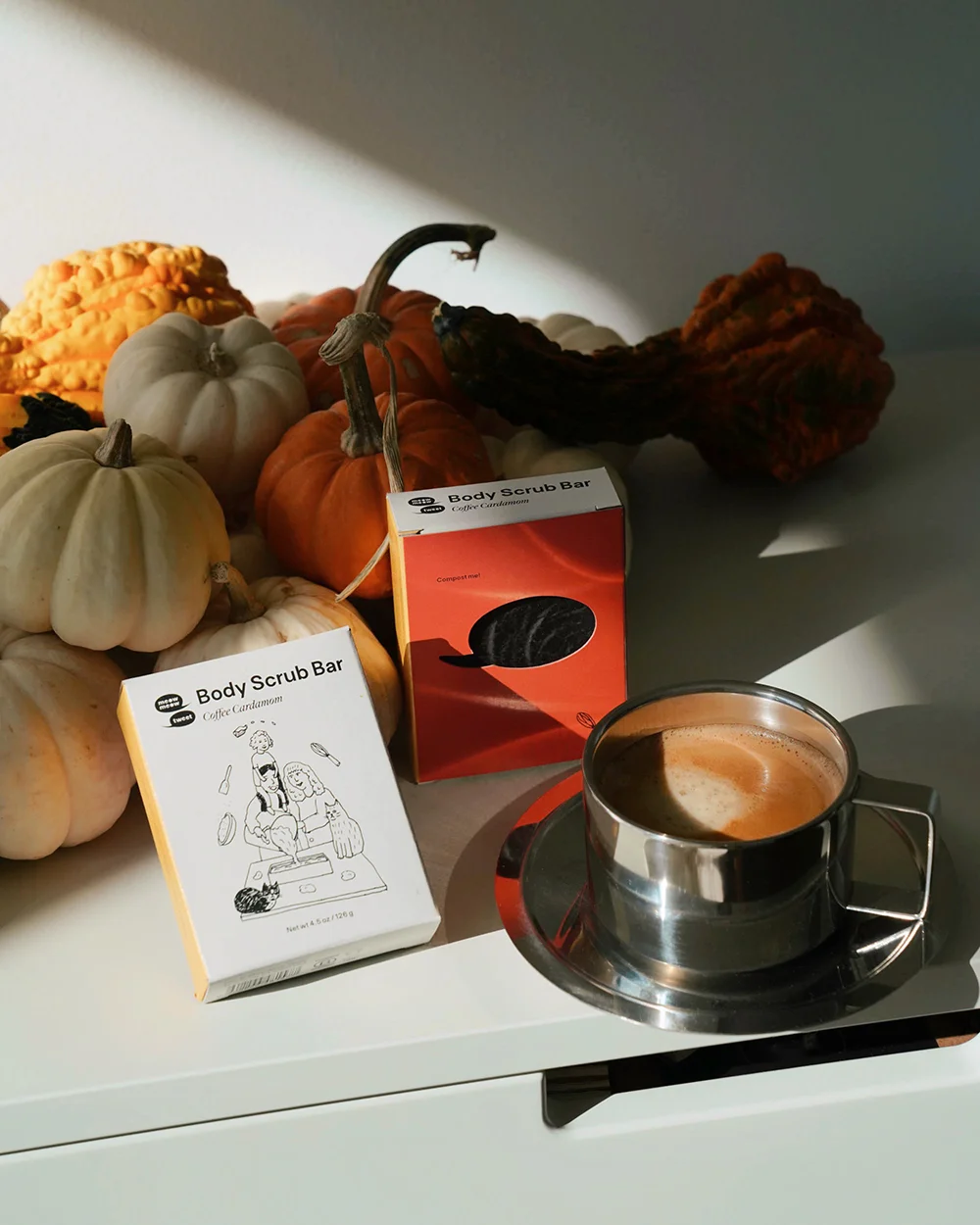 A bar of soap leans against a bunch of small pumpkins and next to a cup of coffee