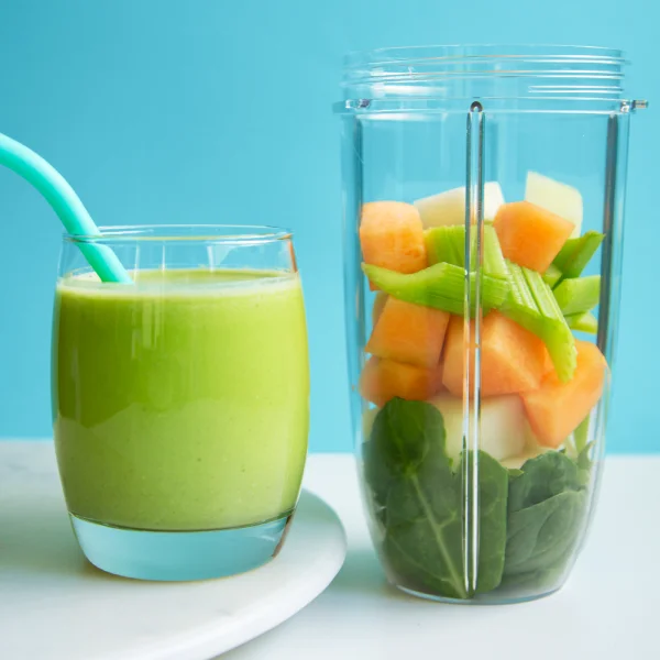 Melon smoothie next to pieces of fruits and vegetables in a cup