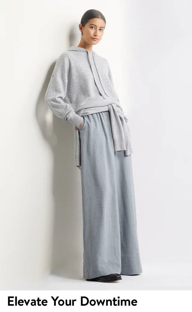 A woman wearing a grey knit hoodie with blue wide-leg pants.