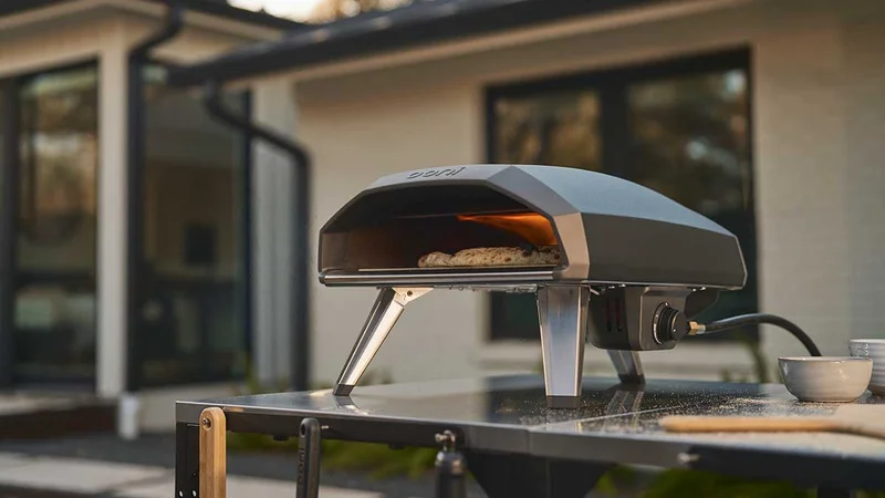 Koda 2 standing on an Ooni table with a pizza being cooked inside of it