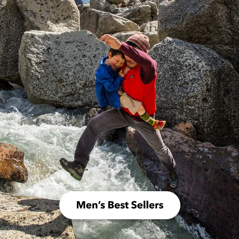 A person jumps over a stream holding their child. Shop Men’s Best Sellers.