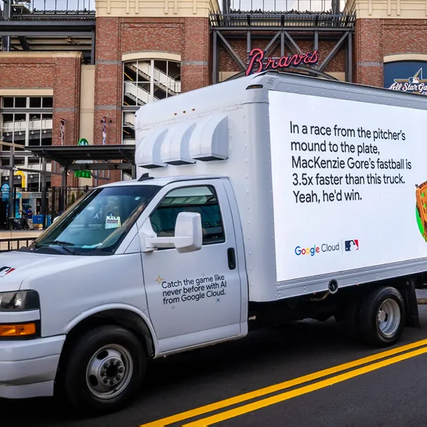 A white Google Cloud box truck with a large advertisement on its side, stating Mackenzie Gore's fastball is 3.5 times faster than this truck, parked in front of a stadium with the word Braves visible.
