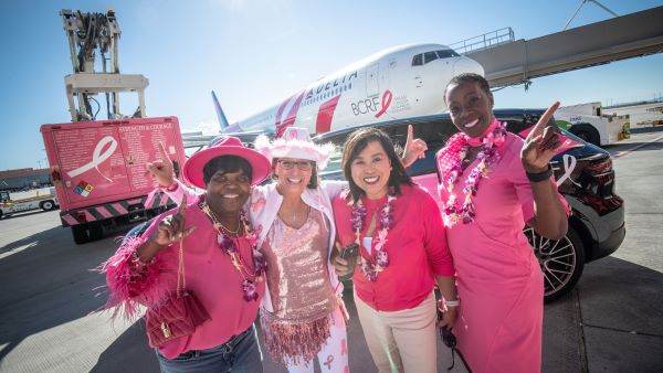 Delta people dressed in all pink pose in front of Delta's Breast One charter plane.