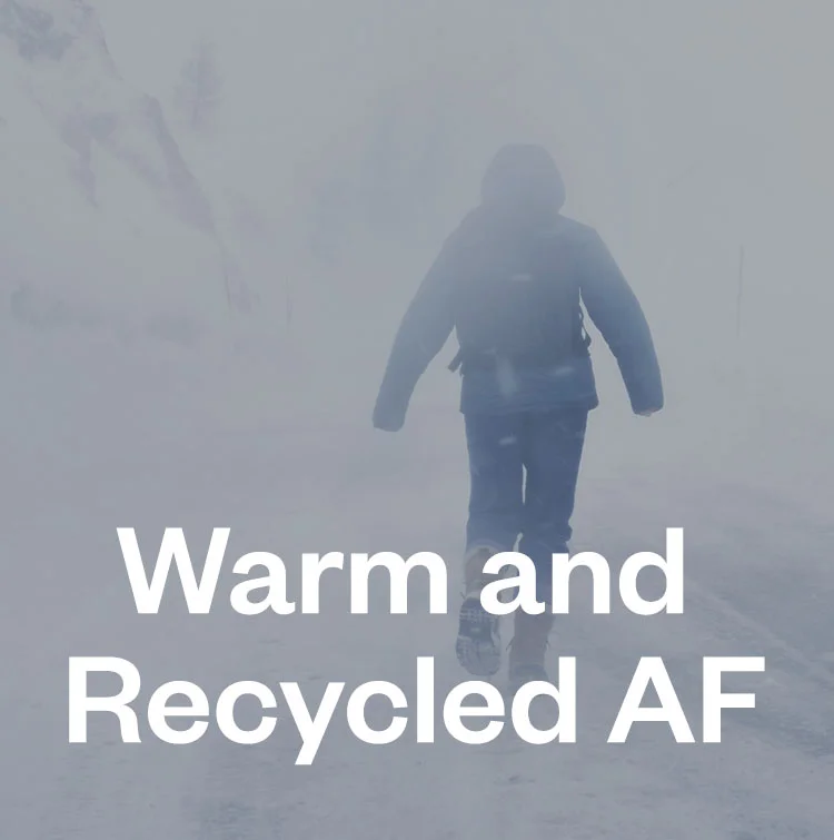 Warm and recycled AF. A person walks in near white-out conditions, hands retracted into the sleeves of their thick jacket.
