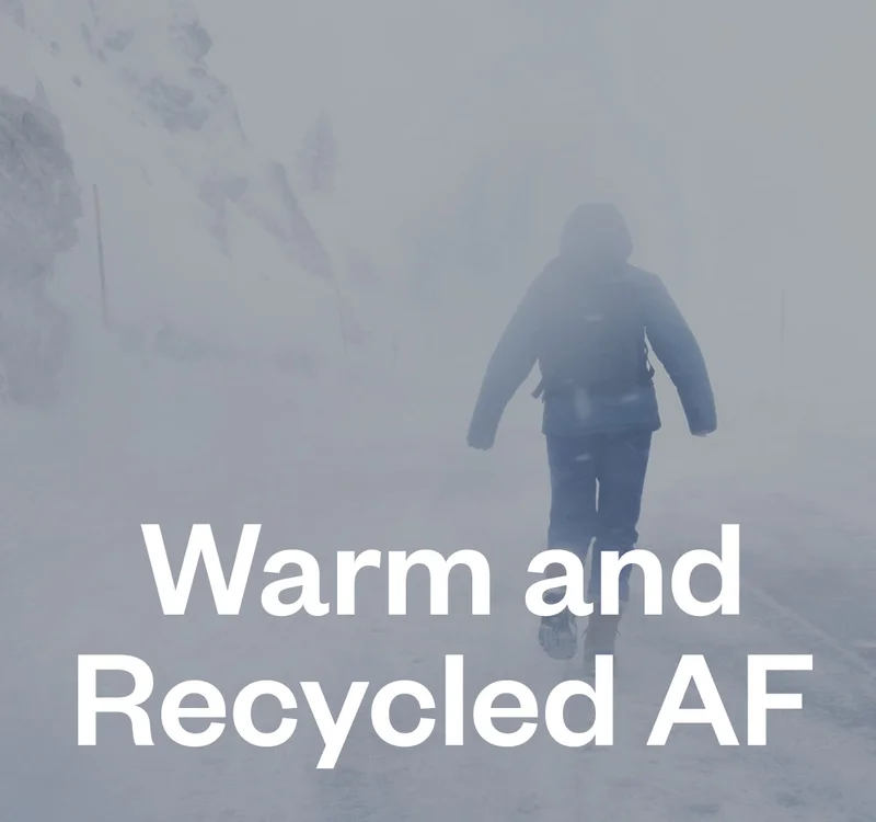 Warm and recycled AF. A person walks in near white-out conditions, hands retracted into the sleeves of their thick jacket.
