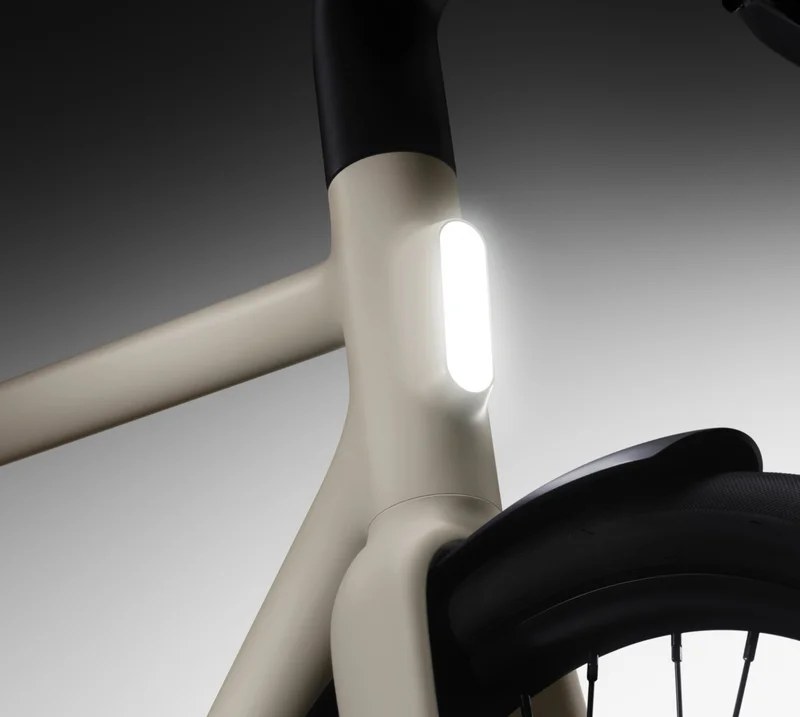Alt Text:  A close-up of a Cowboy e-bike’s head tube, showcasing its integrated front light glowing brightly against a dark gradient background. The sleek frame and smooth lines emphasize the bike’s minimalist design.