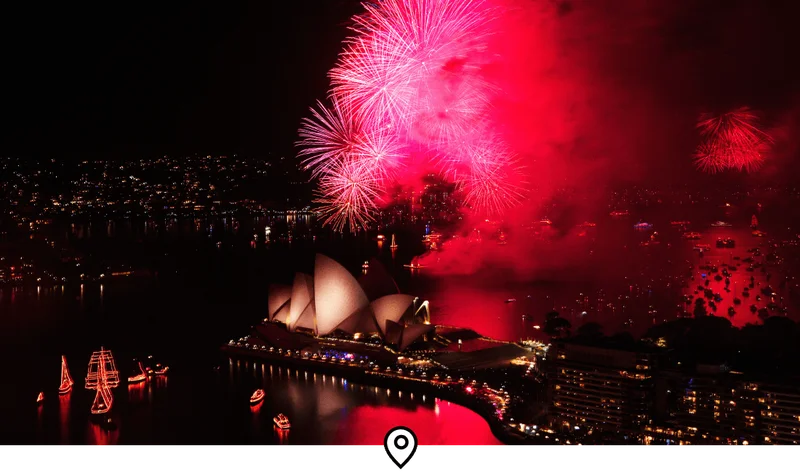 Image Description: An aerial view of a massive fireworks show over the iconic Sydney Harbor skyline