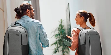 Two people walking and having a conversation. They are each wearing a gray Dell EcoLoop Backpack.