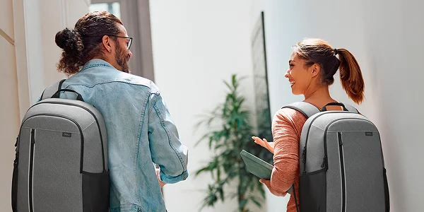Two people walking and having a conversation. They are each wearing a gray Dell EcoLoop Backpack.
